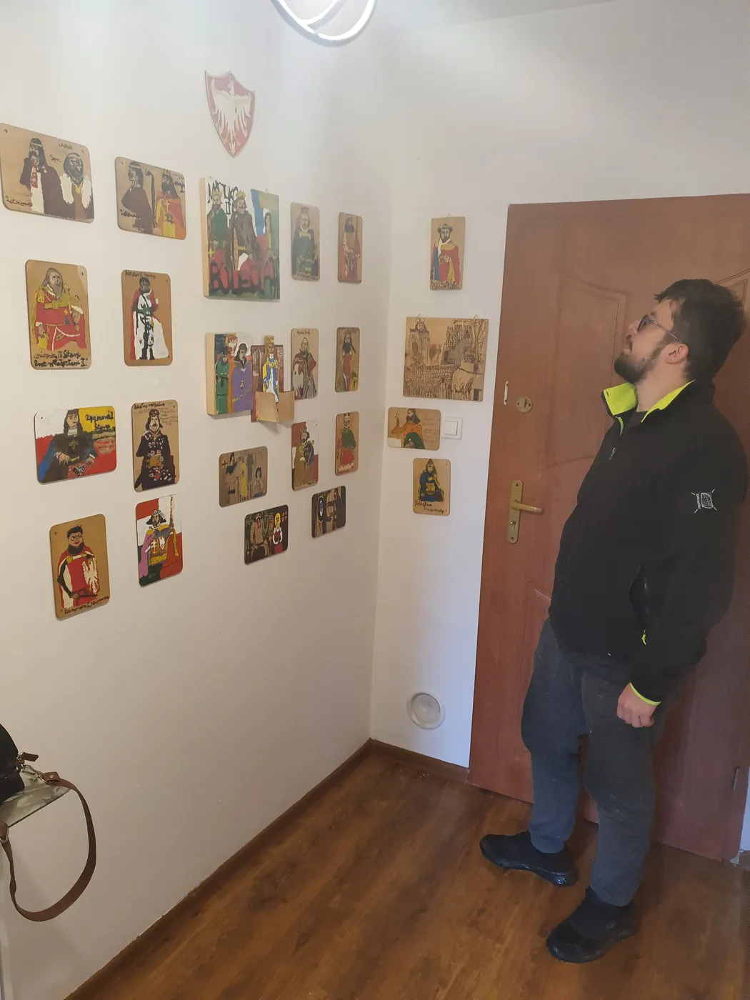 Michał Walczyk patrzy na ścianę zawieszoną małymi portretami na deseczkach