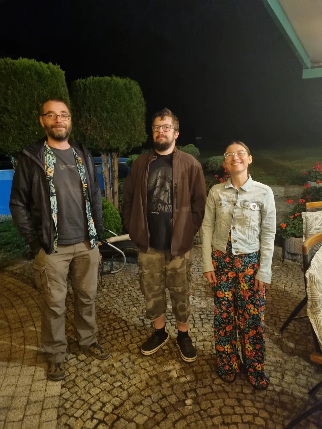 Trzy osoby stoją wieczorem w ogrodzie