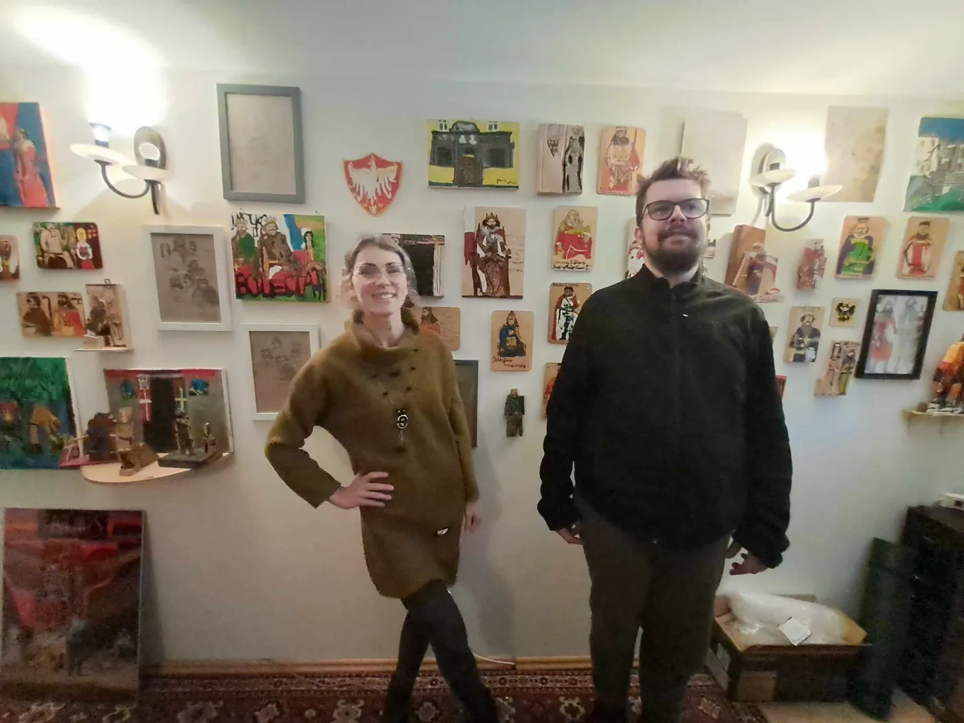 Dwie osoby stoją w pracowni na tle ściany zawieszonej obrazami