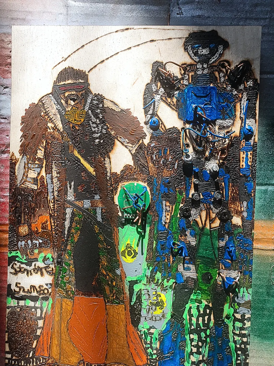 Płaskorzeźba na sklejce: po lewej brodaty mężczyzna w długim płaszczu, po prawej niebieski robot z doklejonymi metalowymi częściami, między nimi zielony świecący element