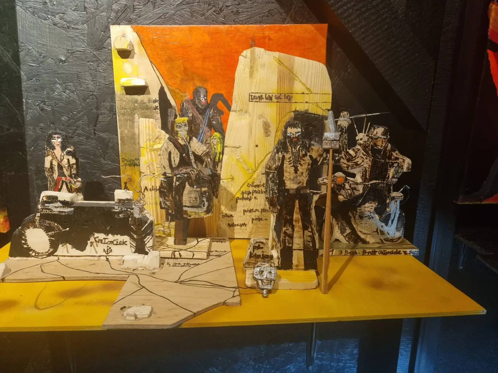 Inside the black exhibition shed, figurines on a lit yellow table