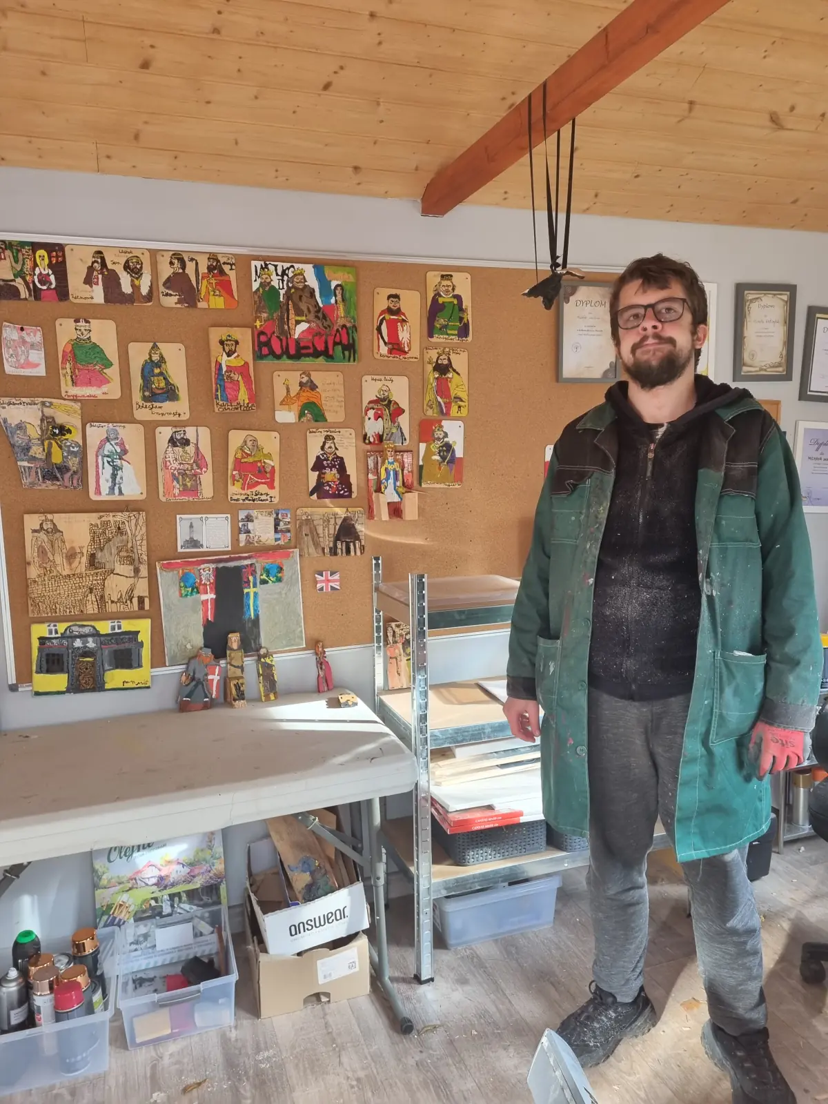 Michał Walczyk w zielonym płaszczu stoi przed ścianą z portretami postaci historycznych
